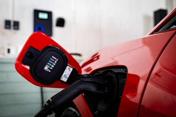 The handle of a smart charger protrudes from the charge port of a red EV.